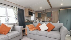 A modern living room with two grey sofas, orange and white cushions, and a small orange pumpkin decoration on the floor. - The Retreat (Morecambe)