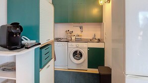 Una cocina compacta con armarios azul verdoso, lavadora, cafetera y un lavabo.