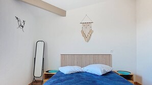 Un dormitorio con una cama, dos mesitas de noche, una lámpara colgante y un adorno en la pared.