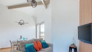 Una sala de estar moderna con un sofá gris, una mesa de comedor y un televisor instalado en una pared de madera.