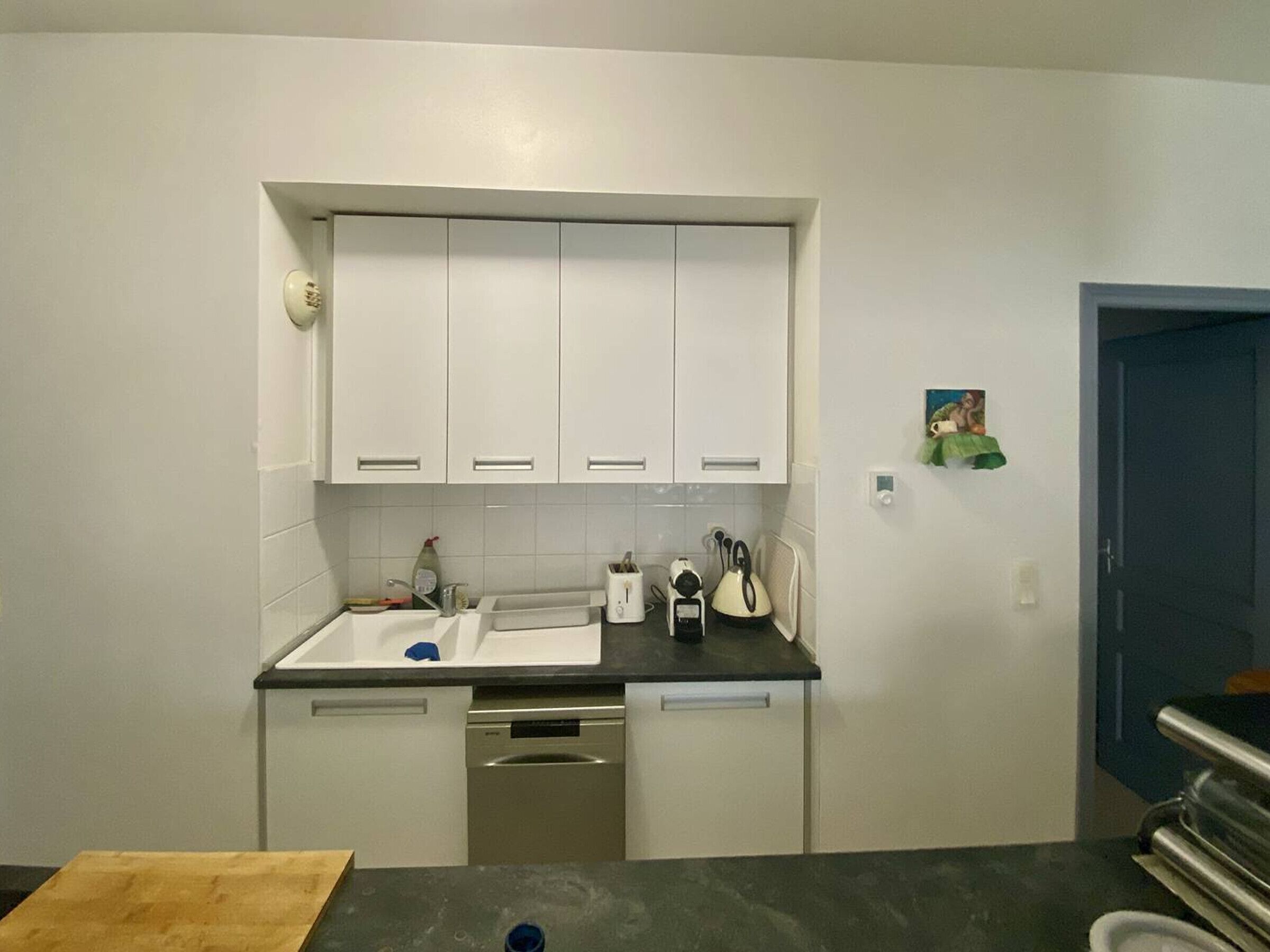 A compact kitchen with white cabinets, a dishwasher, and a countertop with a toaster and kettle.