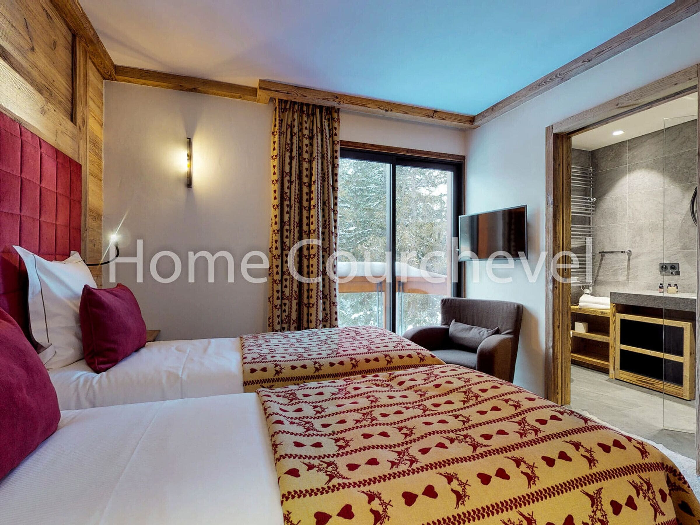 A hotel room with two beds, a wooden headboard, a large window with curtains, a chair, and a bathroom visible through an open door.
