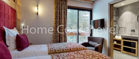 A hotel room with two beds, a wooden headboard, a large window with curtains, a chair, and a bathroom visible through an open door.