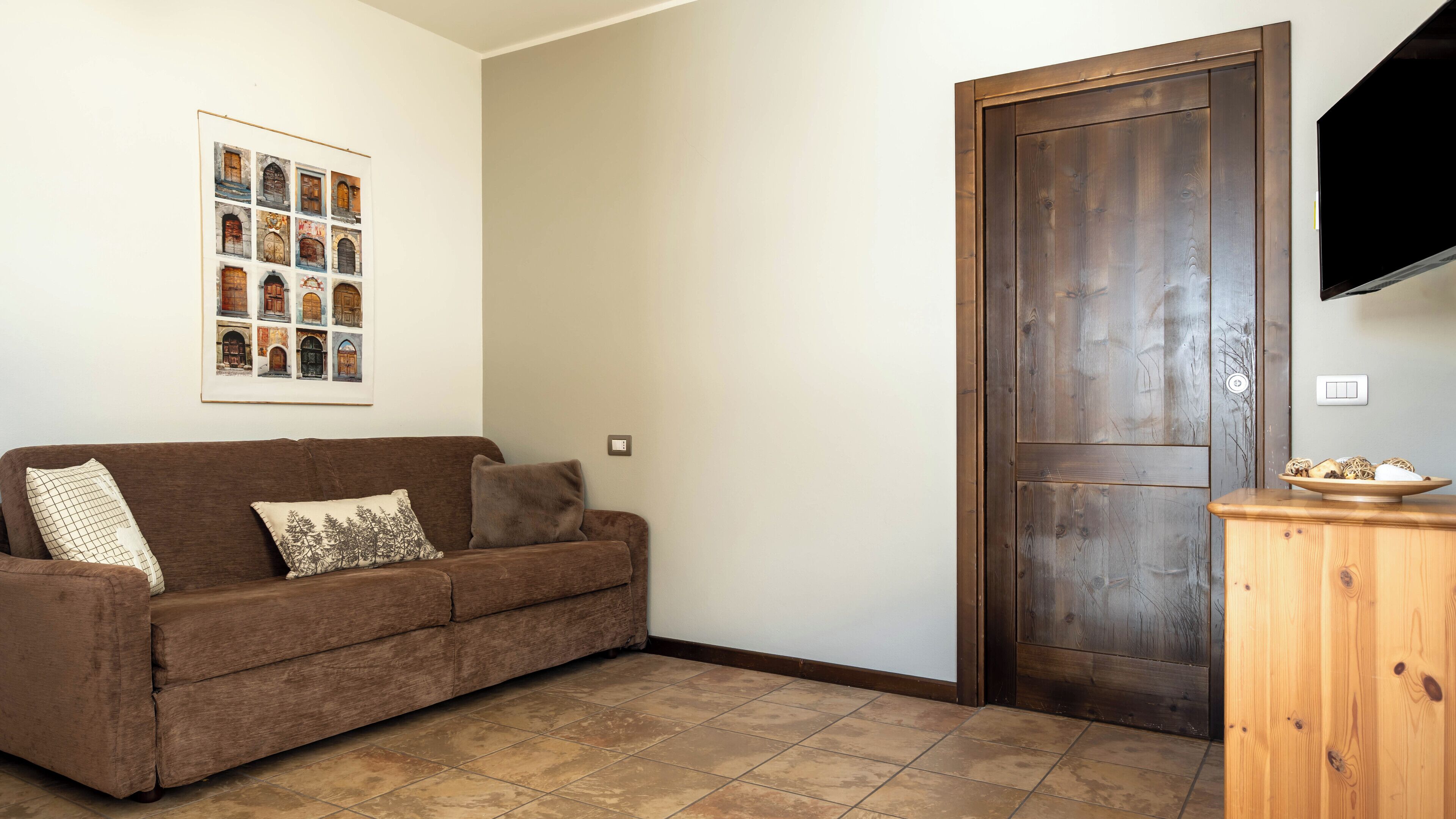 A living room with a brown sofa, a framed picture on the wall, a wooden door, and a small wooden cabinet.