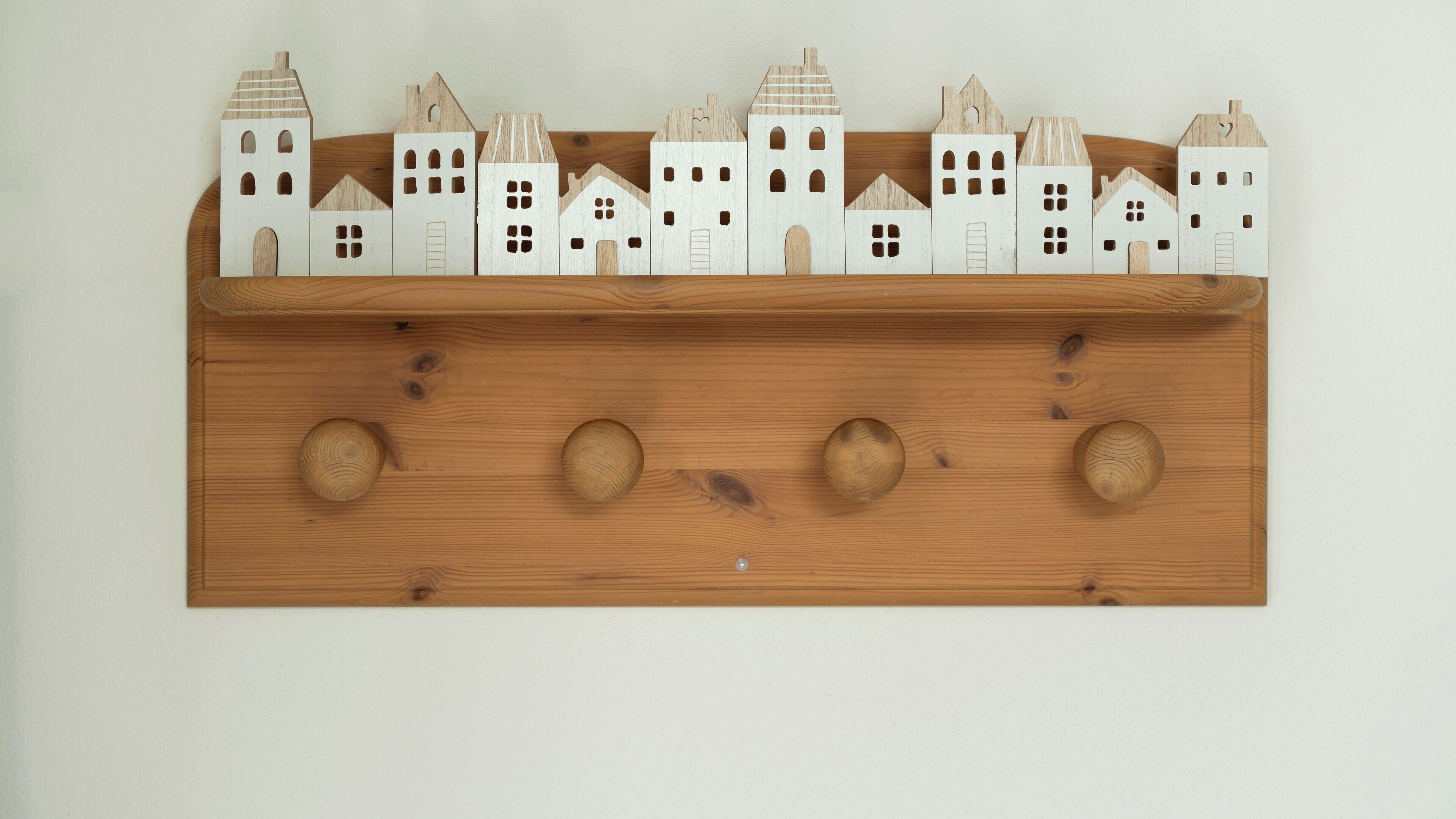 A wooden shelf with white wooden house models and four round wooden knobs.
