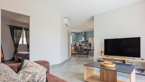 A modern living room with a sofa, a coffee table, and a TV. There is a dining area in the background with a kitchen visible. - Villa Flora with Private Pool, Terrace, and Wi-Fi (Balazuc)