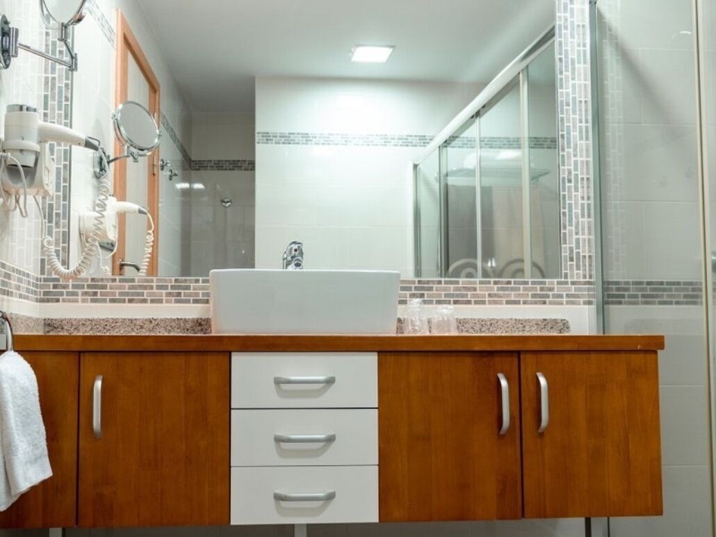 Ein Badezimmer mit Holzwaschtisch, weißem Waschbecken und einer Duschkabine aus Glas.