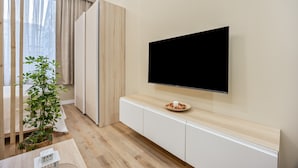 Ein modernes Wohnzimmer mit einem flachbildfernseher an der Wand, einer Holzkommode darunter und einer Zimmerpflanze auf dem Boden.