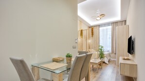 Ein moderner Essbereich mit einem Glastisch, grau gepolsterten Stühlen, Holzboden, Wand-Fernseher und Deckenventilator.