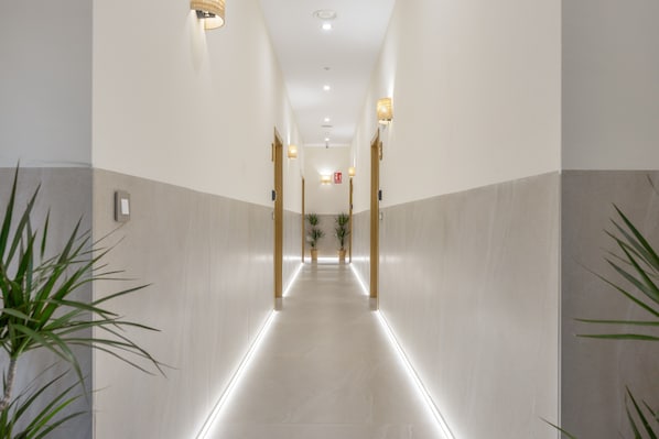 A hallway with a lighted path, potted plants, and a fire exit sign.
