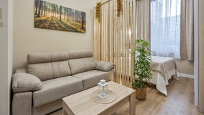 Ein Zimmer mit einer Couch, einem kleinen Tisch mit einer Dekoration, einer Pflanze und einem Bett mit Fenster.