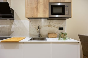 A kitchen with a microwave, sink, wooden cabinets, and a marble backsplash.