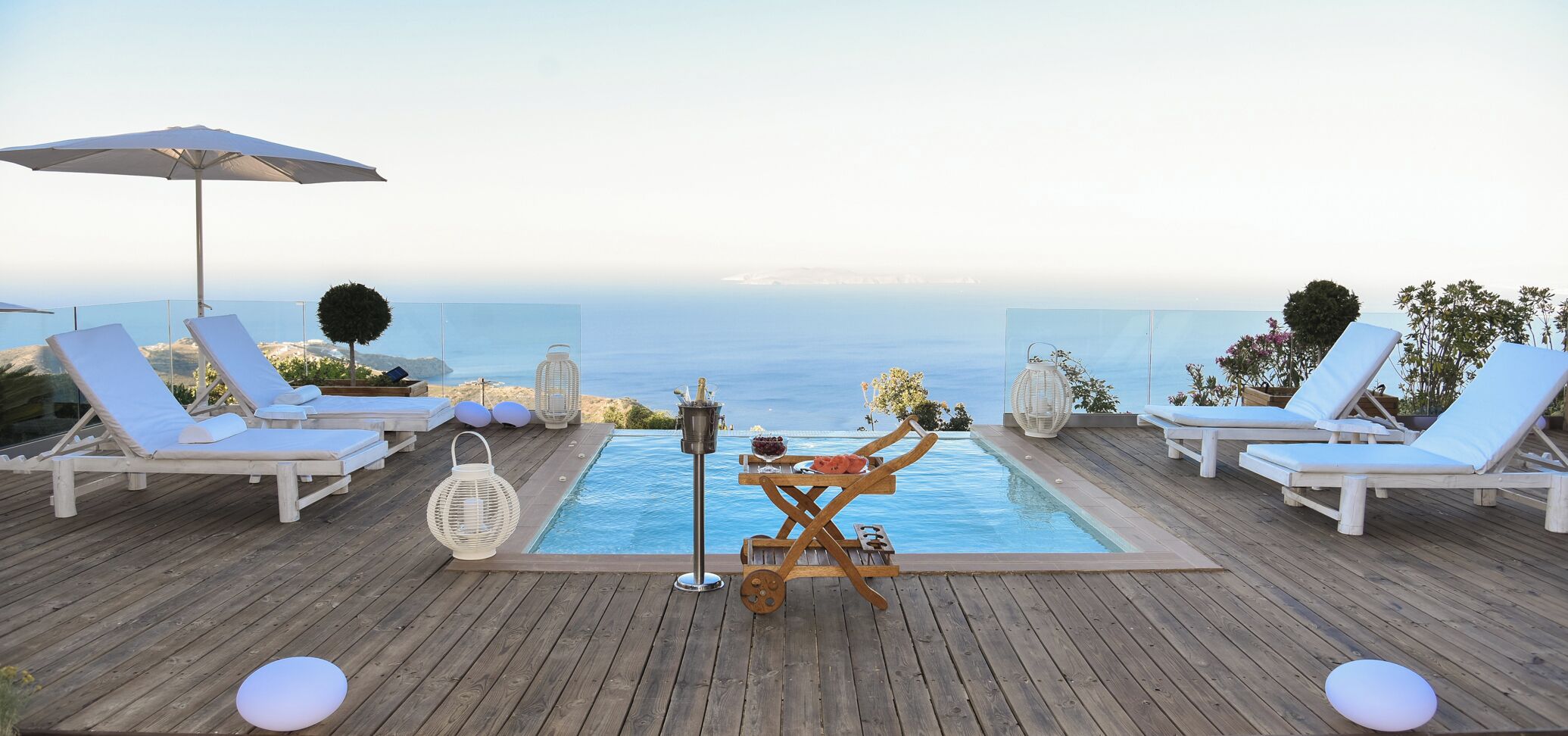 Un terrazzo in legno con piscina, sedie a sdraio e vista sul mare.