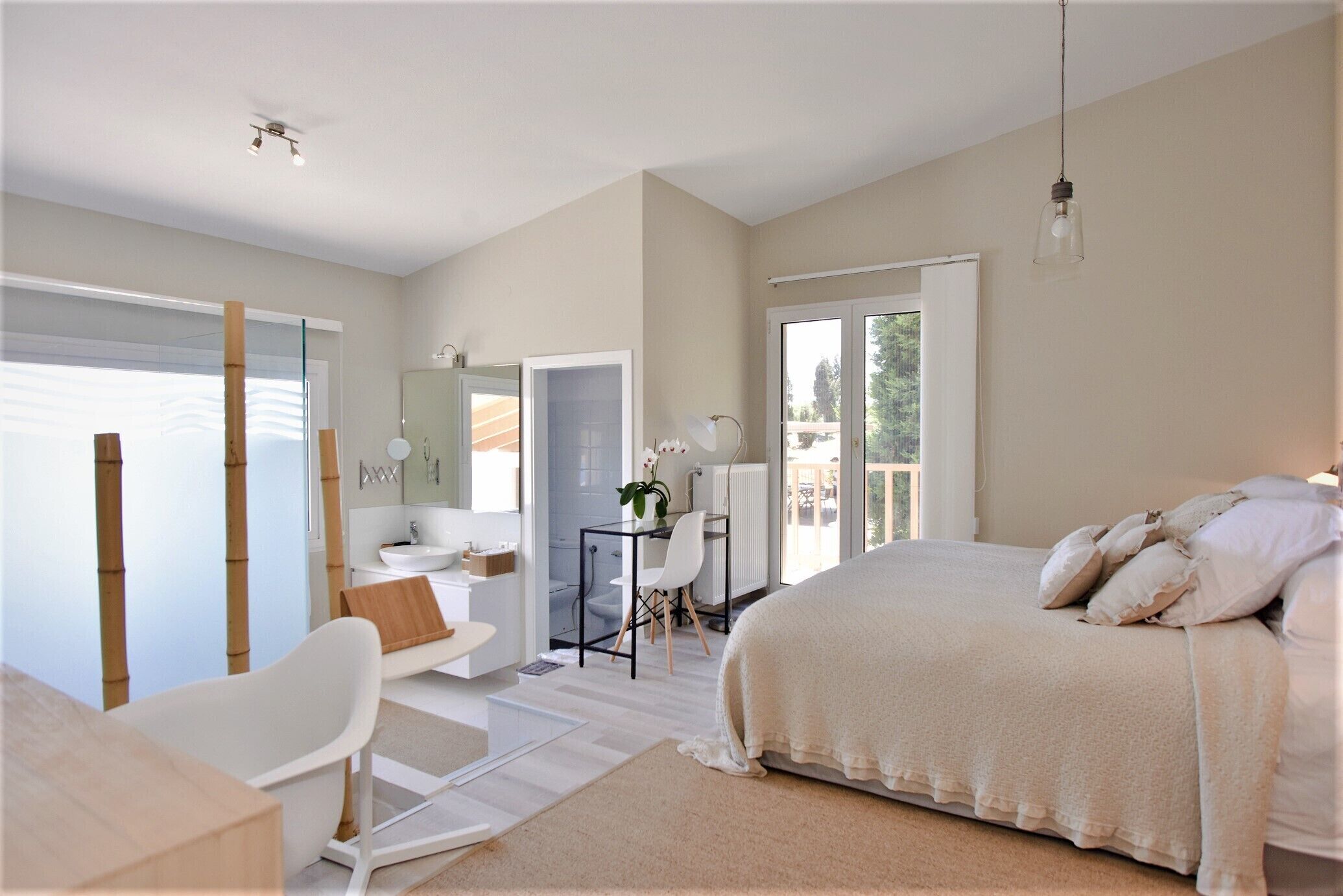 A modern bedroom with a large bed, a desk, a chair, and a bathroom.