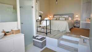 Ein Schlafzimmer mit einem Bett, Nachttischen, einem Beistelltisch, einem Sessel und einem kleinen Tisch mit einer Lampe.