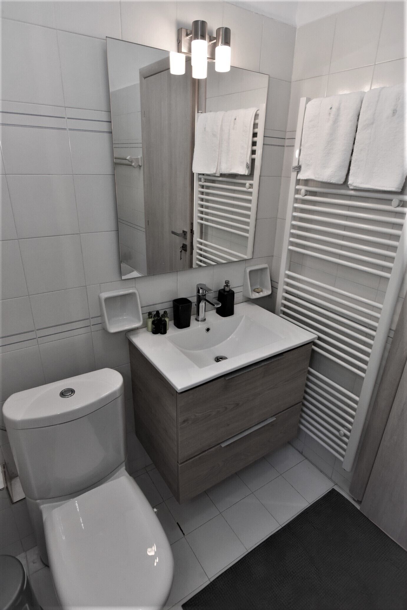 Une salle de bain moderne avec des toilettes blanches, un lavabo surmonté d’un miroir et un porte-serviettes avec des serviettes.