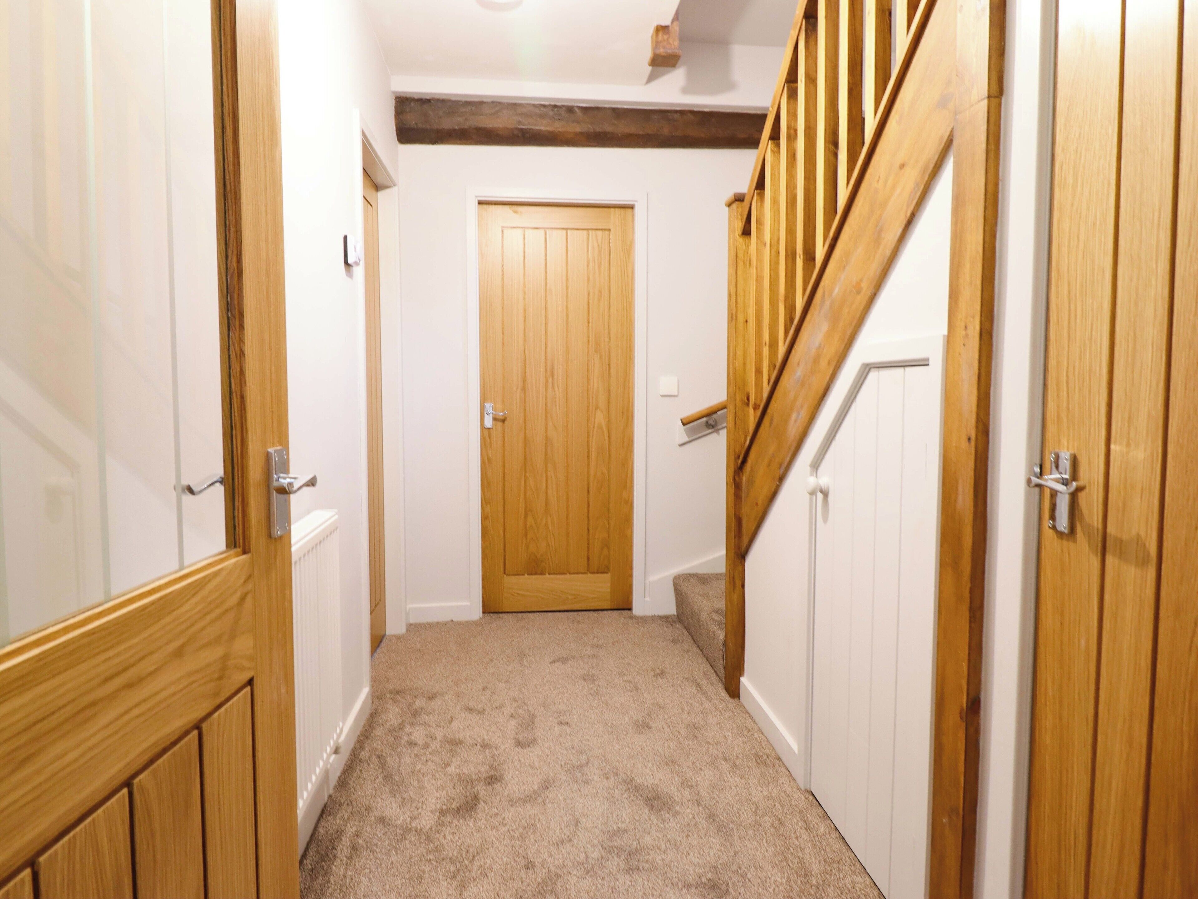 A narrow hallway with wooden doors and a carpeted floor, leading to a wooden staircase.