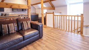 A spacious loft with exposed wooden beams, a leather sofa, a kitchen area, and a view of the outside. - Clegir Bach (Corwen)