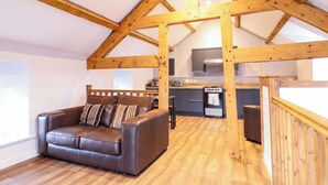 A loft-style room with a wooden ceiling, a brown leather sofa, a kitchen area, and a wooden staircase. - Clegir Bach (Corwen)