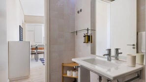 Une salle de bain moderne avec un lavabo blanc, deux robinets, un miroir et un espace douche.