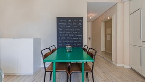 Un coin repas avec une table verte et quatre chaises, un tableau noir avec des inscriptions et un réfrigérateur en arrière-plan.
