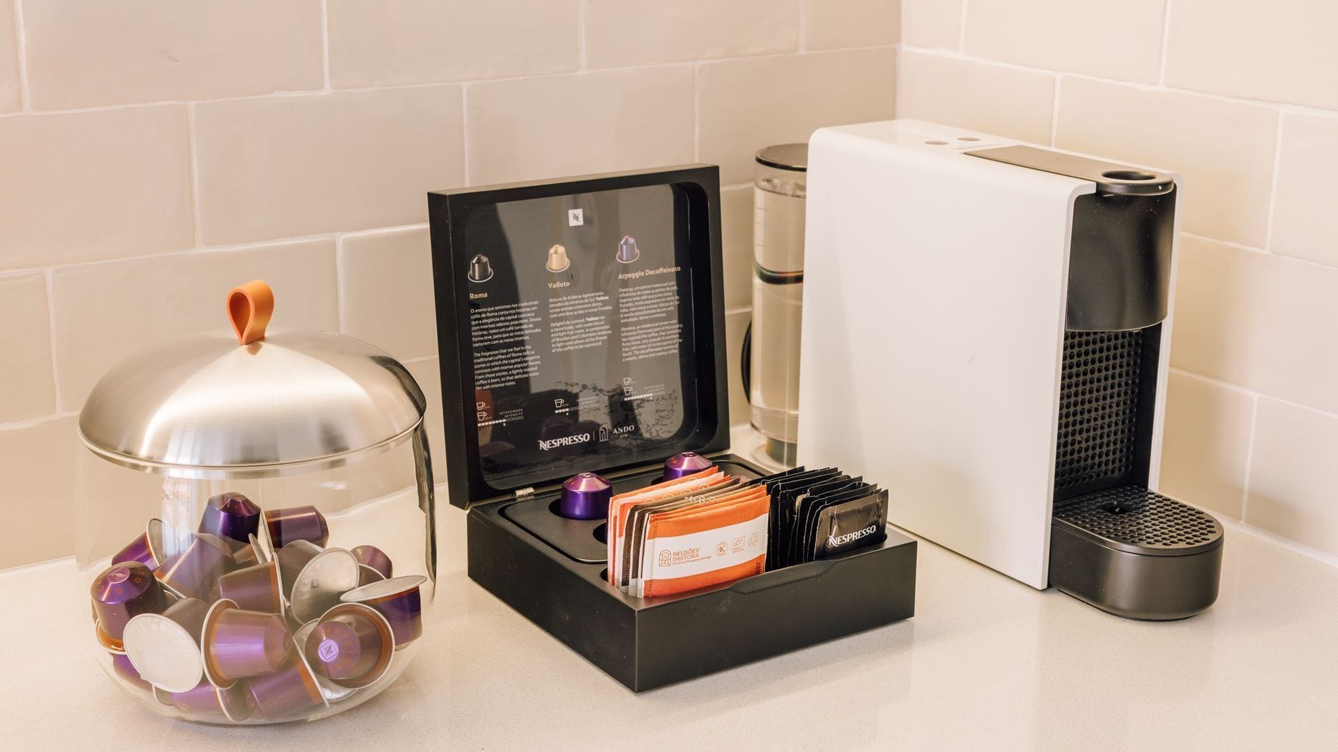 A coffee machine, a glass container with coffee pods, and a booklet on a countertop.