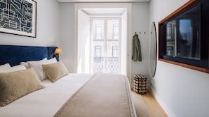 Una camera da letto con un letto, una testiera, una lampada, una finestra, una porta, uno specchio e una TV a parete.