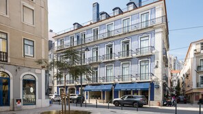 Un edificio de varios pisos con fachadas de diseño azul y blanco, un patio central y una calle con coches aparcados.