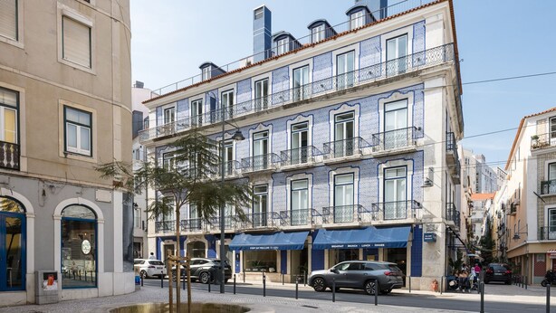 Un edificio de varios pisos con fachadas de diseño azul y blanco, un patio central y una calle con coches aparcados.