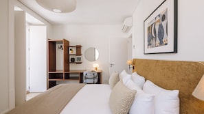 A hotel room with a bed, a desk, a chair, a wardrobe, a mirror, a lamp, and a framed picture on the wall. - Ando Living - Two Bedroom Superior Apartment (Lisbon)
