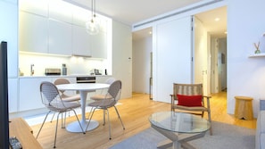 A modern kitchen with white cabinets, a dining table with wireframe chairs, and a glass coffee table. - Ando Living - Douradores House - 201 (Lisboa)
