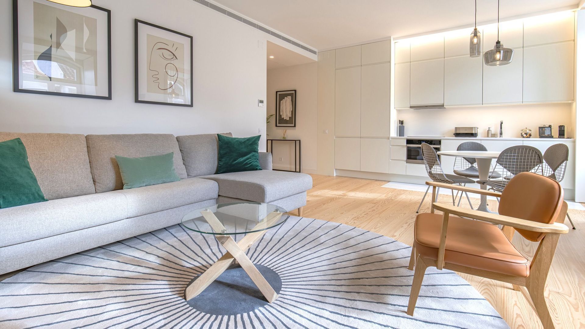 A modern living room with a grey sofa, green cushions, a glass coffee table, and a patterned rug.