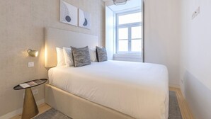 A neatly arranged bedroom with a large bed, a bedside table, and a wall-mounted lamp. - Ando Living - Douradores House - 203 (Lisboa)
