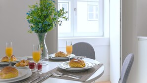 A breakfast setting with croissants, orange juice, and a vase of flowers. - Ando Living - Douradores House - 203 (Lisboa)