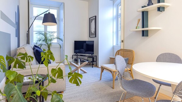 Ein modernes Wohnzimmer mit einer Couch, einem Esstisch, Stühlen, einem Fernseher und einem großen Fenster.