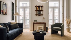 A living room with a sofa, armchair, coffee table, and a bookshelf. - Ando Living - São Nicolau House - 101 (Lisboa)
