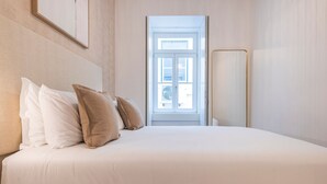 A hotel room with a bed, pillows, a door, and a window. - Ando Living - Douradores House - 301 (Lisboa)