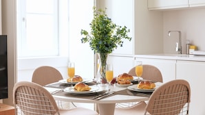 A breakfast setting with a table, chairs, a vase with flowers, and plates with croissants and juice glasses. - Ando Living - Douradores House - 301 (Lisboa)