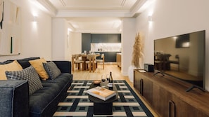 Ein modernes Wohnzimmer mit Sofa, Couchtisch und Fernseher. Es gibt einen Essbereich mit Tisch und Stühlen.
