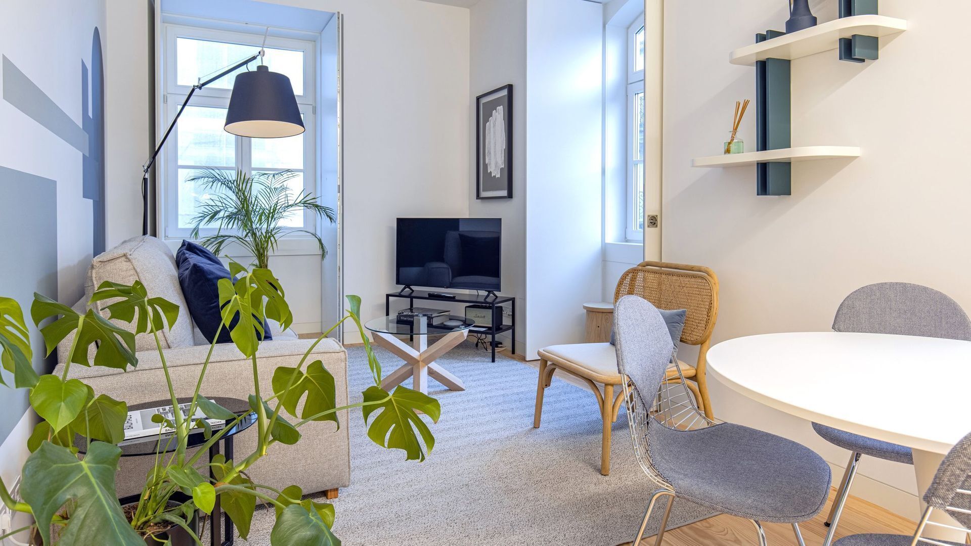 Una sala de estar moderna con sofá, mesa de comedor, sillas, televisor y un ventanal grande.