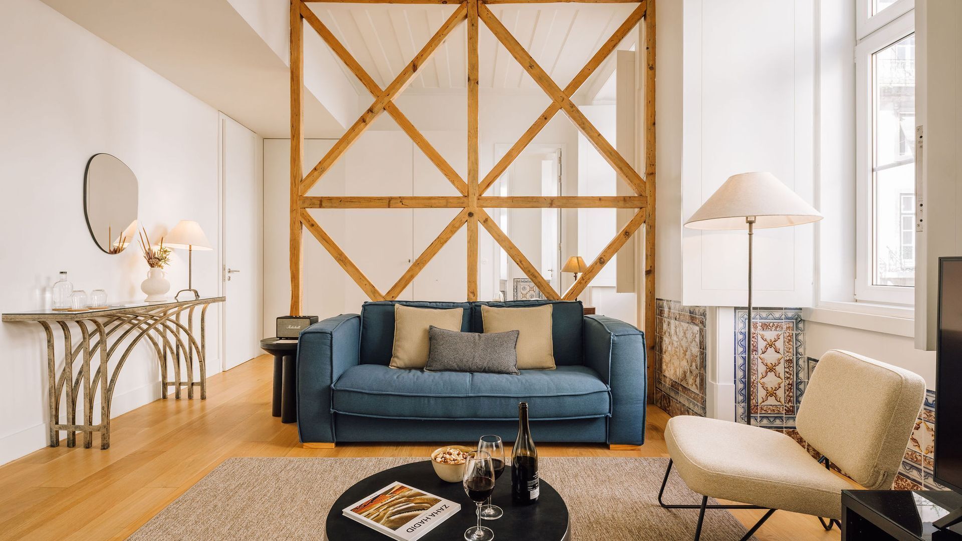 A modern living room with a blue sofa, a coffee table with wine glasses and a bottle, a side table with a lamp, and a large wooden partition.