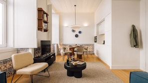 A modern living room with a TV, sofa, and coffee table, a dining area with chairs and a table, and a kitchen with white cabinets. - Ando Living - Santa Justa 79 House - 201 (Lisboa)