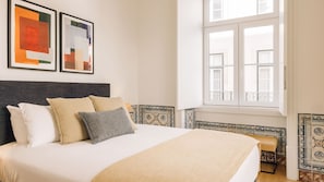 A neatly made bed with pillows, a window with a view, and two abstract paintings on the wall. - Ando Living - Santa Justa 79 House - 201 (Lisboa)