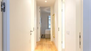 Un couloir étroit, doté d’un plancher en bois, mène à une chambre à coucher qui contient un lit et une fenêtre.