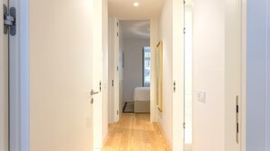 A narrow hallway with wooden flooring leading to a bedroom with a bed and a window. - Ando Living - Douradores House - 401 (Lisboa)