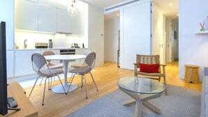 Une cuisine moderne avec des meubles blancs, un coin repas doté d’une table en verre et de chaises en métal, et un plancher en bois.