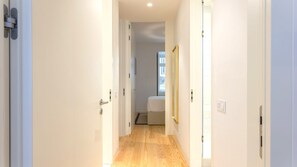 Ein schmaler Flur mit Holzboden führt zu einem Schlafzimmer mit Bett und Fenster.