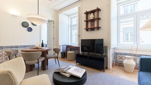 Uma sala de estar com televisão, mesa de jantar com cadeiras, estante de livros e janela com vista.
