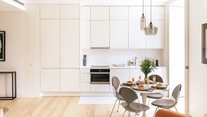 Una cucina moderna con mobili bianchi, forno integrato e zona pranzo con tavolo rotondo e sedie in metallo.