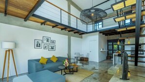 A spacious living area with a blue sofa, a coffee table, and a TV. There is a staircase leading to an upper level with a balcony. - Urban Oasis Loft by GORO (Kabupaten Badung)